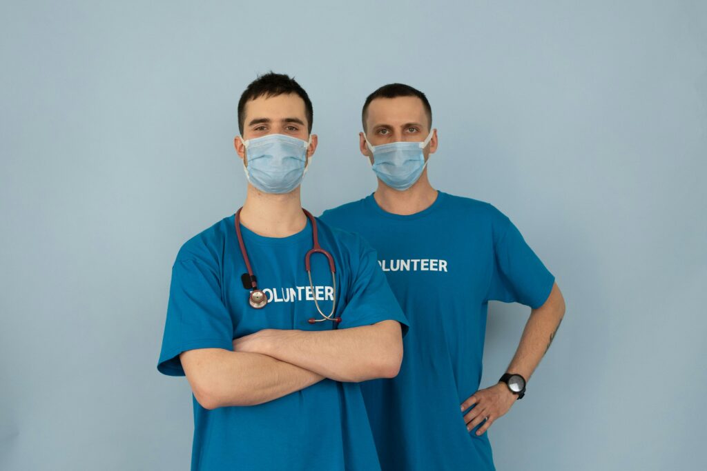 Two men in blue volunteer shirts and masks, symbolizing teamwork and safety.